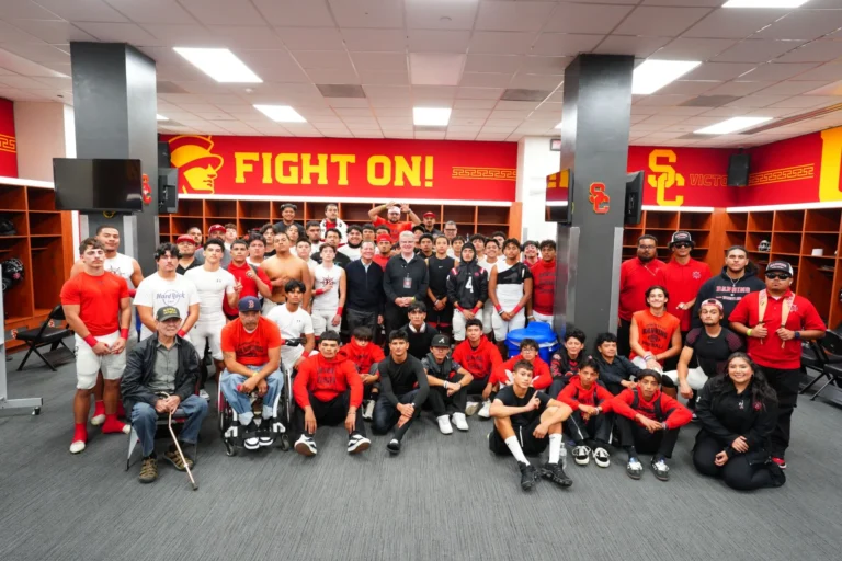 A group of people in red and black clothing pose in a sports locker room with "Fight On!" signs on the walls.